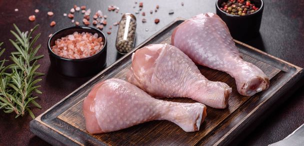 Fresh raw chicken legs with spices, salt and herbs on a cutting board. Preparing a dish for baking in the oven - Fotografie, Obrázek