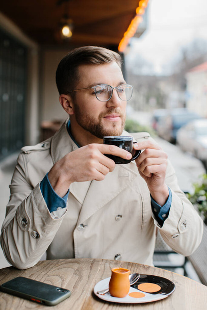 Молодий чоловік п'є каву у відкритому кафе
. - Фото, зображення