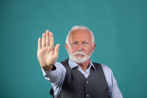 Portrait of mature man with white hair and beard showing stop sign, hand gesture, against blue background in studio - Photo, Image