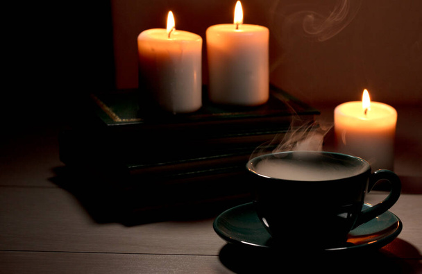 Filiżanka gorącej kawy z zielonym dymem, książki i płonące świece. Stół biurkowy w odcięciu zasilania - Zdjęcie, obraz