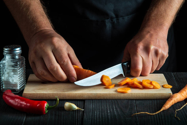 Séf vágás sárgarépa zöldségleves az étterem konyhájában. Egy közeli kép a szakács kezéről munka közben. Sárgarépa diéta. - Fotó, kép
