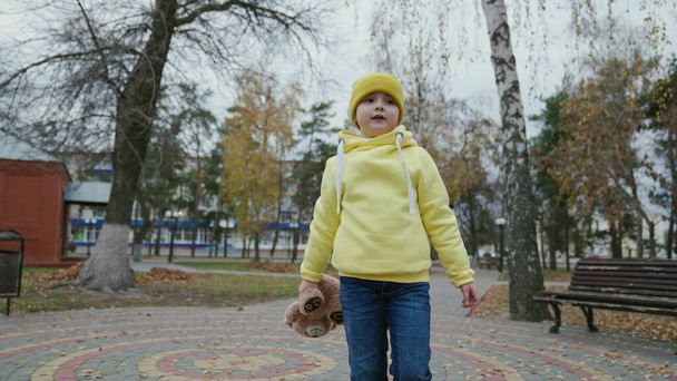 小さな女の子、秋の公園で散歩のためのテディベアを持つ子供。遊び場でテディベアを持つかわいい赤ちゃん。屋外でテディベアを持つ孤独な女の子。テディは子供、健康な子供を手にする - 写真・画像