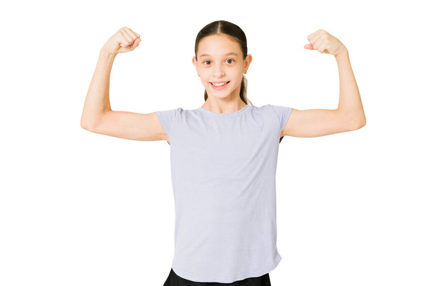 Poder feminino. Retrato de uma menina alegre sorrindo e sentindo-se forte ao mostrar seu bíceps - Foto, Imagem
