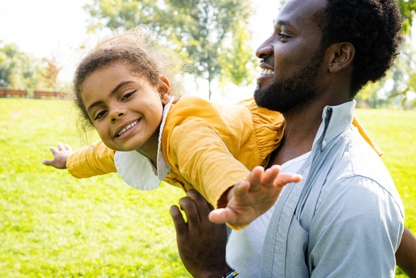 Beautiful happy african american family bonding at the park - Black family having fun outdoors, dad playing with his cute daughter - Foto, Imagen