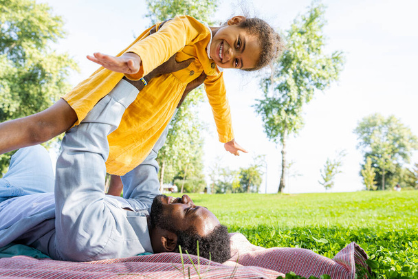 Beautiful happy african american family bonding at the park - Black family having fun outdoors, dad playing with his cute daughter - Zdjęcie, obraz