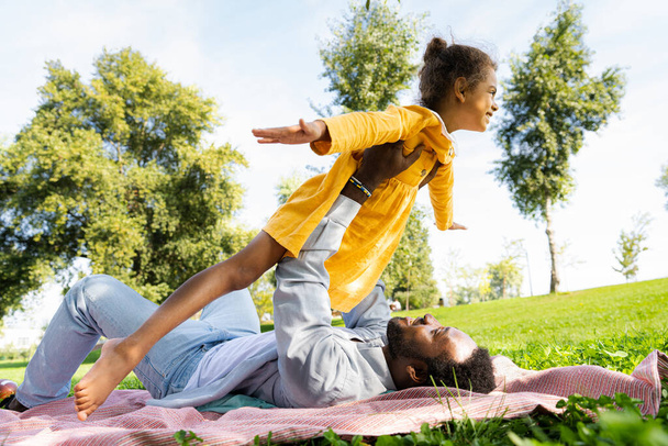 Beautiful happy african american family bonding at the park - Black family having fun outdoors, dad playing with his cute daughter - Foto, imagen