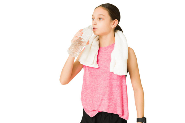 Fit beautiful girl with a towel taking a break from her workout and drinking water. Tired active teen resting from exercise - Foto, immagini