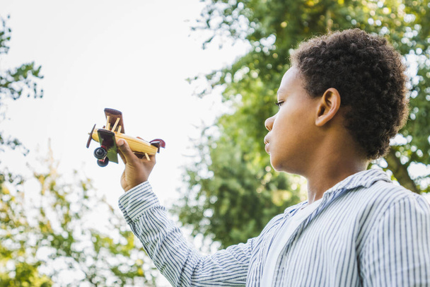Beautiful happy african american family bonding at the park - Black family having fun outdoors, cute young boy playing with airplane toy - Photo, Image