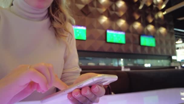 Женщина работает на мобильном телефоне в ресторане, экраны телевизоров с футболом - Кадры, видео