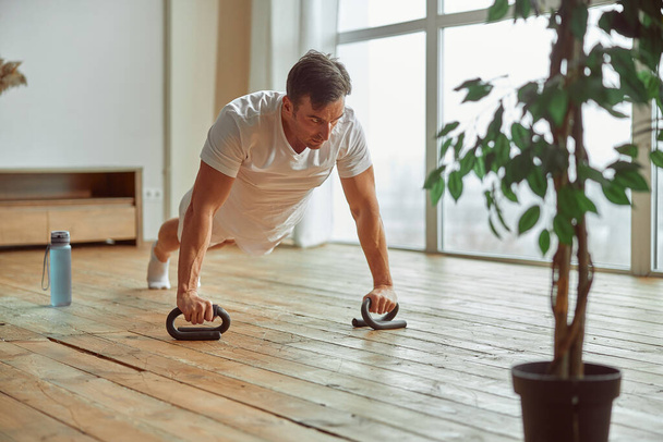 Sporty man doing push ups with equipment indoors - Photo, Image
