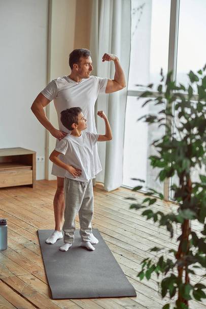 Спортивные отец и сын демонстрируют мышцы в помещении - Фото, изображение