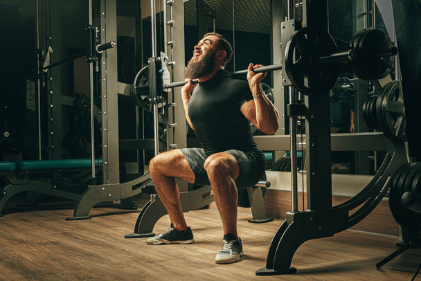 Fit man doing squats in a training machine - 写真・画像