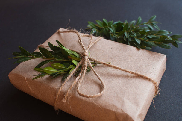 Caixa de presente artesanal com nó natural com folhas verdes sobre fundo preto. Conceito de venda em fundo escuro - Foto, Imagem