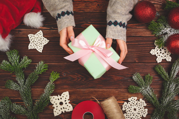 Hands in sweater holding a gift on wooden table with Christmas decorations - Photo, image