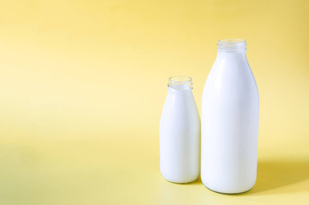 Two glass bottles of milk on a yellow background. A liter and 0.5 liters of milk in glass bottles on a colored background place for text - Fotografie, Obrázek