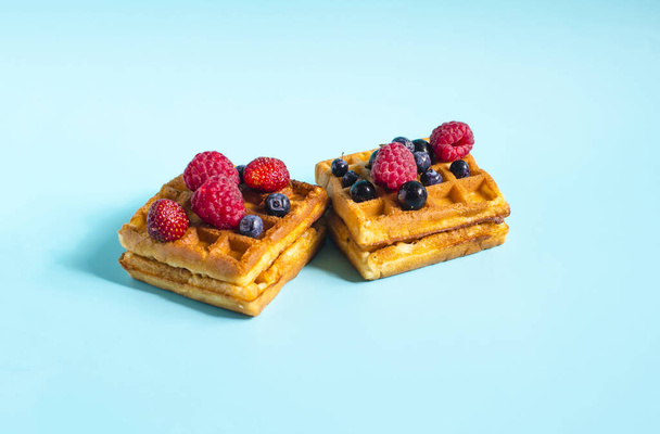 Fresh waffles with different berries of black and red color on a blue background close-up. Homemade cakes crispy waffles on a colored background - Fotó, kép