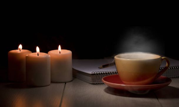 mesa con velas encendidas cuaderno de lápiz, taza amarilla con vapor de humo - Foto, Imagen