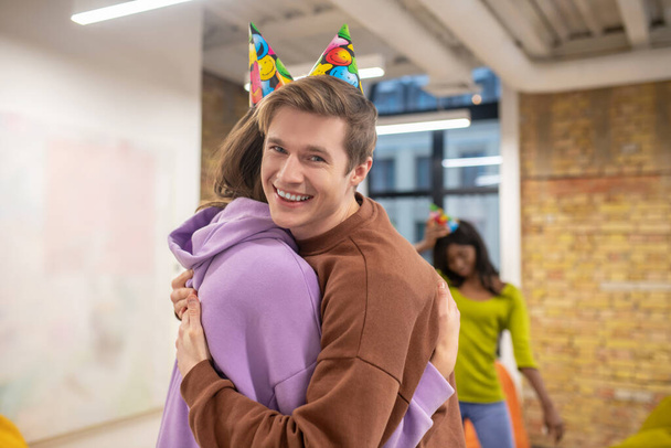 A young guy hugging his colleagues and congartulating her with her bday - 写真・画像