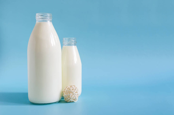 Two glass bottles of milk on a bright blue background. One liter and 0.5 liters of milk in glass bottles on a colored background space for text - Fotografie, Obrázek