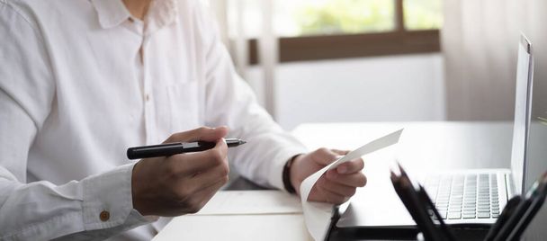 Обрезанная рука человека, пишущего список, делающего заметки в блокноте, работающем или изучающего онлайн с ноутбуком у дома - Фото, изображение