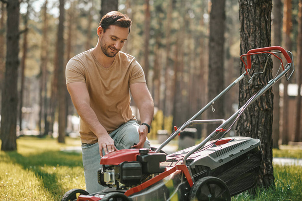 Experienced gardener crouched near lawn mower - Photo, image