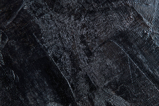 Fond créatif sombre - toile de lin rugueuse inégalement recouverte d'apprêt noir, reflets de lumière. Tonifiant, flou, mise au point sélective.  - Photo, image