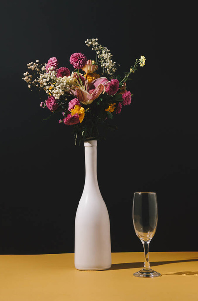 テーブルの上に様々な秋の花やガラスとワインボトルの静物画。自然概念。花の挨拶カード。色とりどりの花の背景. - 写真・画像