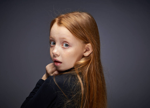 red-haired girl with freckles on her face in a black sweater posing - Foto, afbeelding