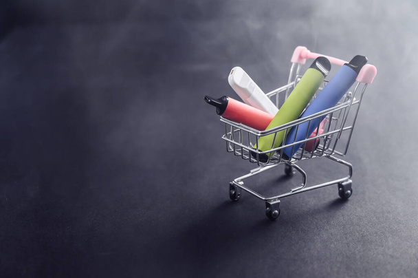 Disposable vapes in a shopping cart on a black background. Modern electronic cigarettes. - Photo, Image