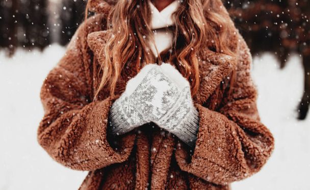 Krásná mladá žena ve sněhobílém zimním lese. Holka v načechraných rukavicích, čepici a kabátě. Vánoční les, stromy na rozmazaném pozadí. Zkřížené ruce kvůli chladnému počasí. Kvalitní fotografie - Fotografie, Obrázek