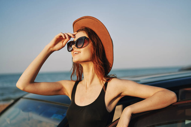 cheerful woman in sunglasses and a hat on the ocean near the car - Foto, imagen