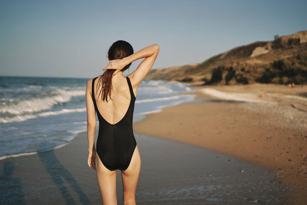 woman walks along the sandy shore in a black swimsuit sun tropics - Fotografie, Obrázek