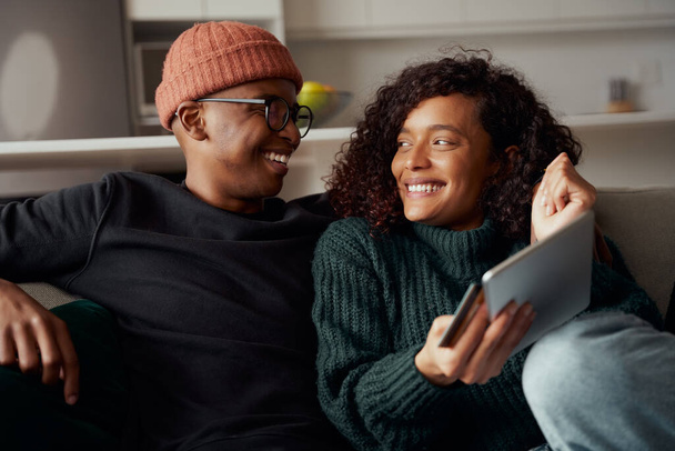 Multi-ethnic couple excited about online purchase made using a tablet sitting on sofa in lounge - Photo, Image