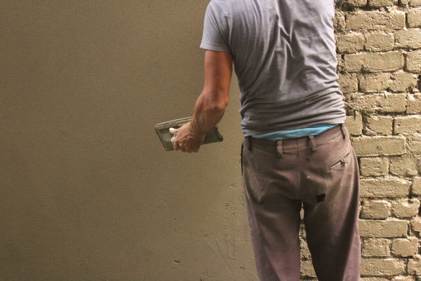 Indian construction worker repairing an old brick wall by applying fresh cement on it - Fotó, kép