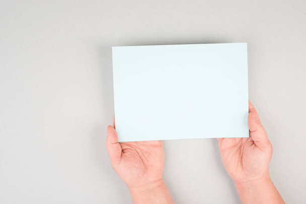 Woman holds a blank sheet of paper, grey colored background, empty copy space for text, minimalism - Foto, afbeelding