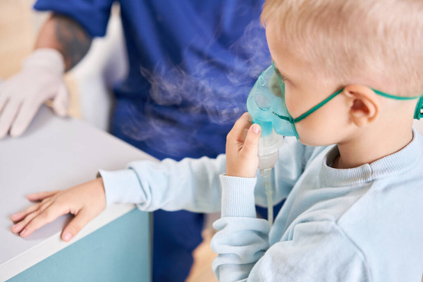 A pediatrician diagnoses lung disease and provides treatment. Breathe the medicine through a nebulizer inhaler.. Portrait of adorable little boy visiting doctor. - Фото, зображення