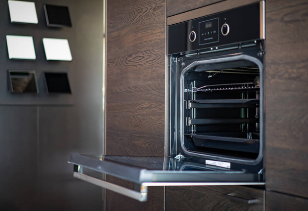 Modern minimaal ovengebouw met houten meubels in de keuken met volledig groene bokeh glas raam naast voor kopieerruimte reclame ontwerp. - Foto, afbeelding