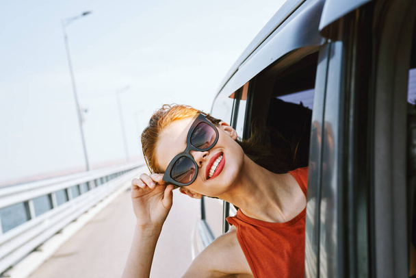 vrouw die uit het autoraam kijkt en een zonnebril draagt reizen levensstijl - Foto, afbeelding