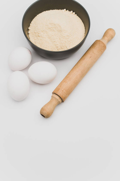wooden rolling pin white eggs and dark gray bowl with wholegrain flour on white background with copy space - Foto, imagen