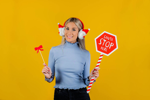Beautiful girl  having fun at a party with photo objects like bows, funny winter headphones and stop sign on yellow background. New year and fun party concept - Photo, Image