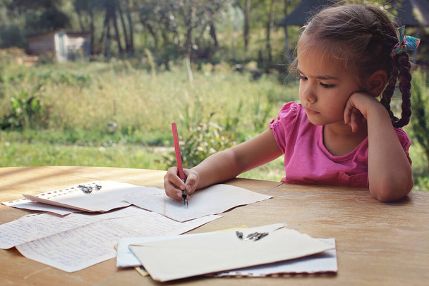 Retro en vintage concept. Een klein meisje dat een brief schrijft met inkt pen, oude enveloppen. - Foto, afbeelding