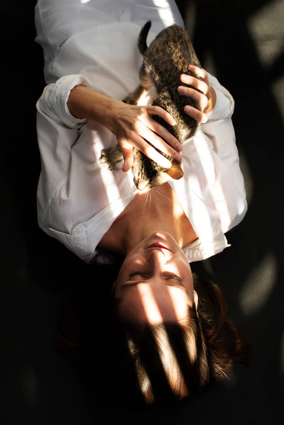 young woman in a white shirt is lying and holding a kitten in her arms. - Fotografie, Obrázek