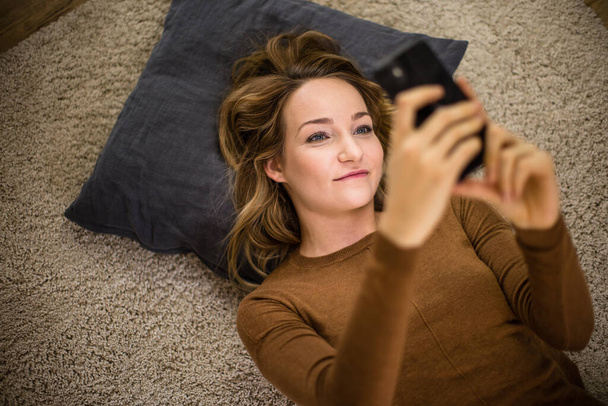 Ładna, młoda kobieta używająca smartfona w domu - Zdjęcie, obraz