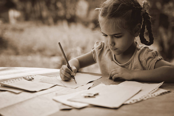 Ретро и винтажная концепция. Маленькая девочка пишет письмо чернильной ручкой, старые конверты - Фото, изображение