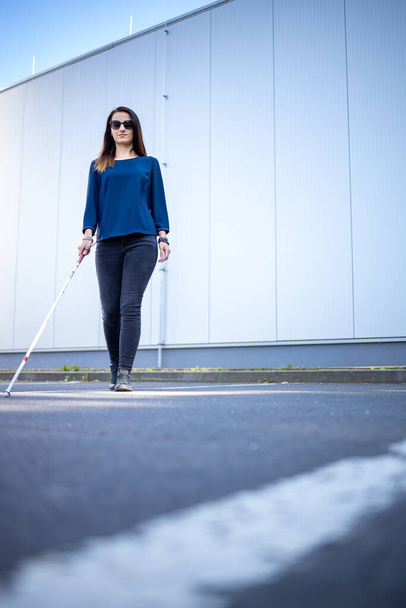 Сліпа жінка ходить по міських вулицях, використовуючи свою білу тростину, щоб краще орієнтуватися в міському просторі і безпечно дістатися до місця призначення
 - Фото, зображення