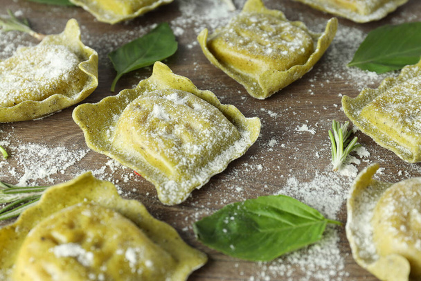 Raw ravioli with flour and basil on wooden background - Фото, изображение
