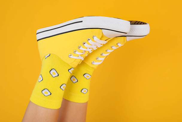 Patas femeninas en calcetines con huevos y zapatillas de deporte sobre fondo amarillo - Foto, imagen