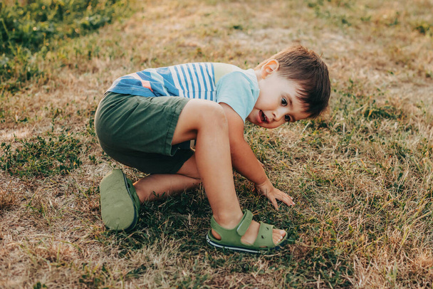 Retrato de um menino caucasiano que caiu no parque e tenta se levantar. Infância cheia de aventuras. Férias passadas fora - Foto, Imagem