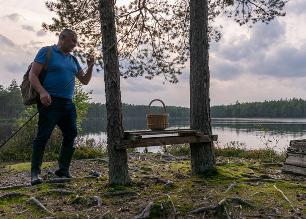 pescador con una caña de pescar en la orilla de un lago pantano, vegetación vegetal característica pantano, bosque de pinos en la orilla del lago, otoño - Foto, Imagen