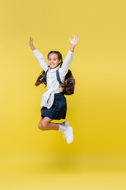 Cheerful schoolgirl with backpack jumping on yellow - Фото, изображение